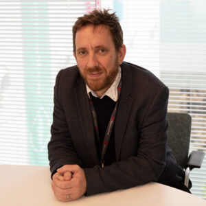 Photo of Prof Neil Hall sitting at a table wearing a dark blazer.